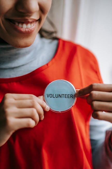 Close-up of a smiling volunteer holding a badge in a bright setting.